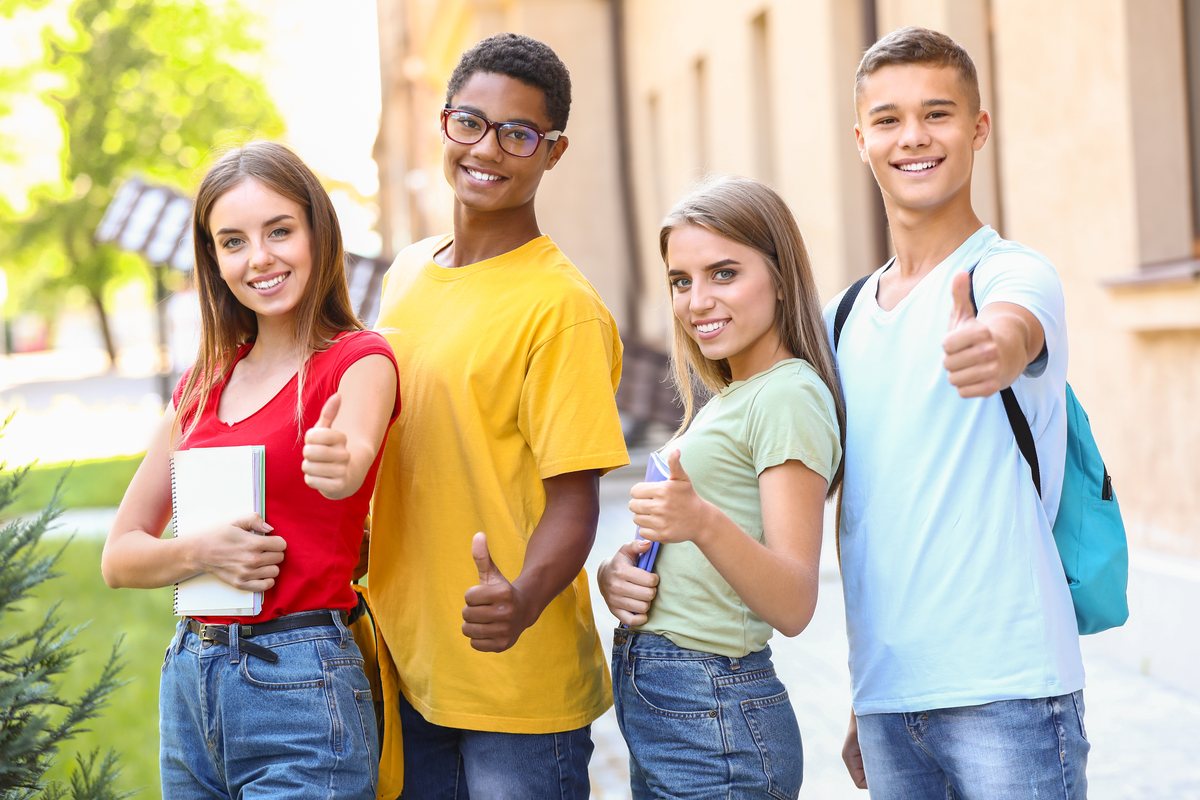 Quattro studenti sorridenti con il pollice alzato davanti alla scuola