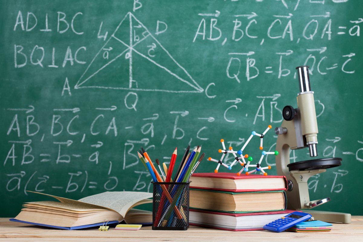 Libri, microscopio e materiale didattico davanti a una lavagna con formule