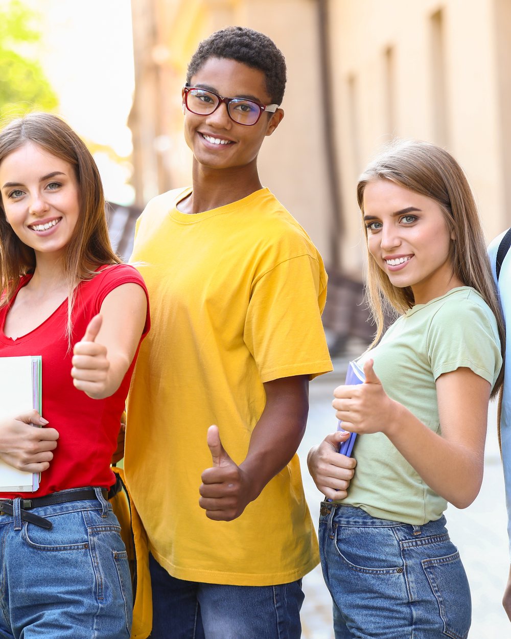 Quattro studenti sorridenti con il pollice alzato davanti alla scuola